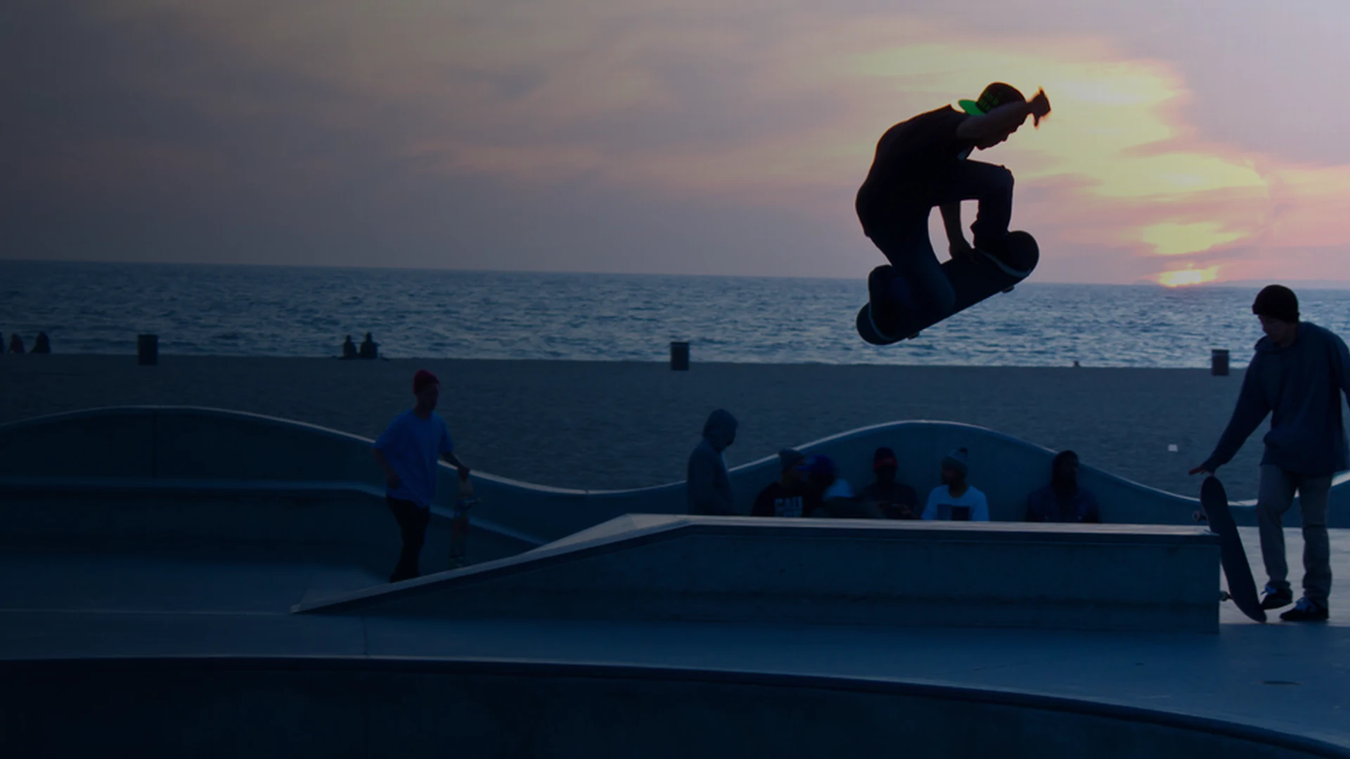 Skateboarder catching air above a seaside skatepark at sunset