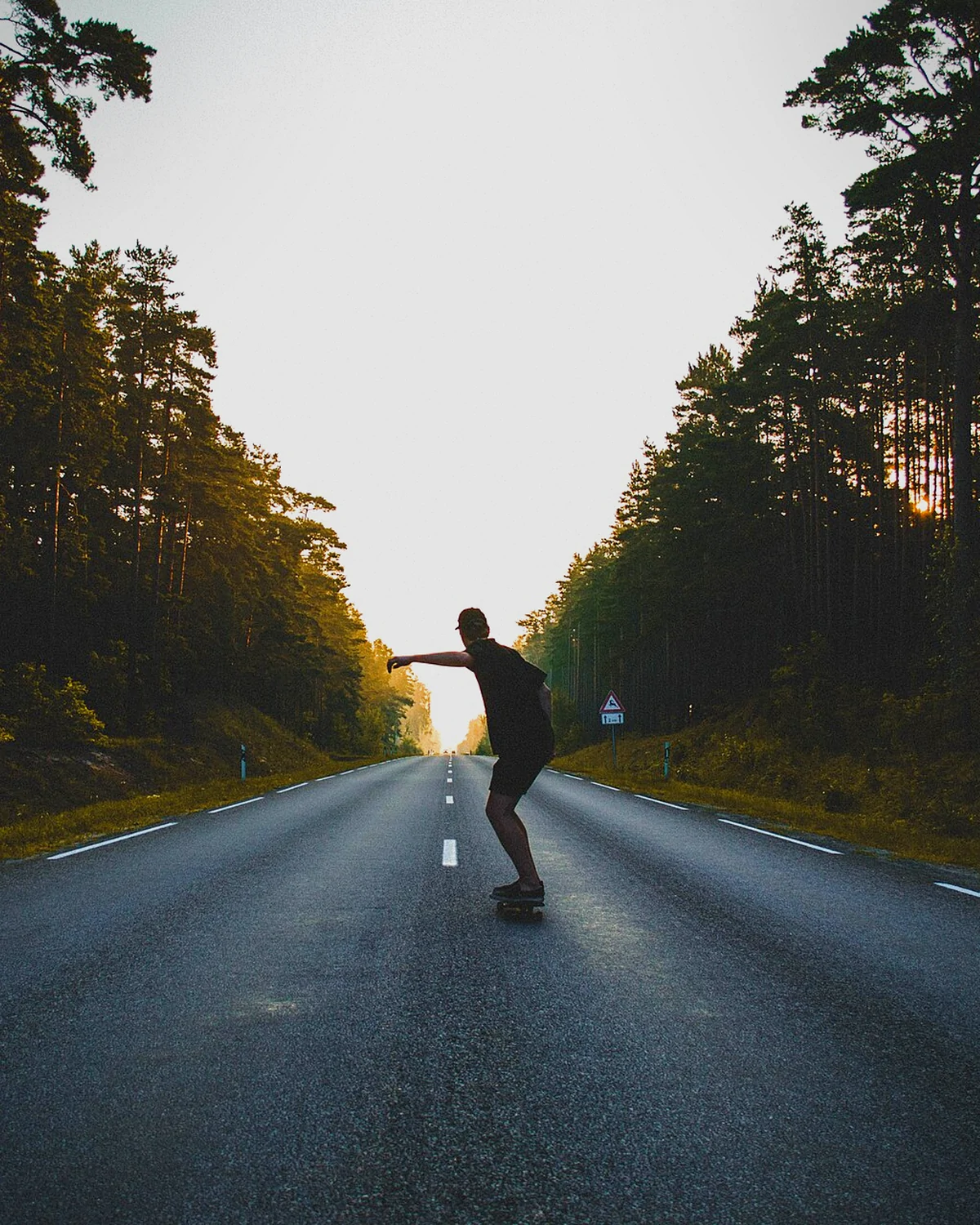 Skateboarder carving down an open road at sunset